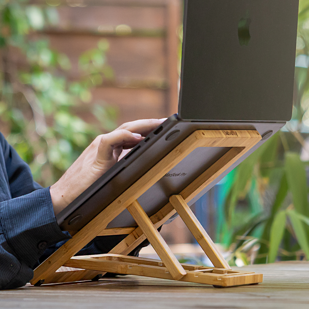 A hand typing directly on a laptop keyboard while the laptop rests on the Levelty bamboo stand