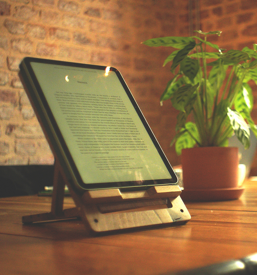 An iPad in portrait mode resting on the Levelty bamboo stand, beside a leafy plant in a terracotta pot